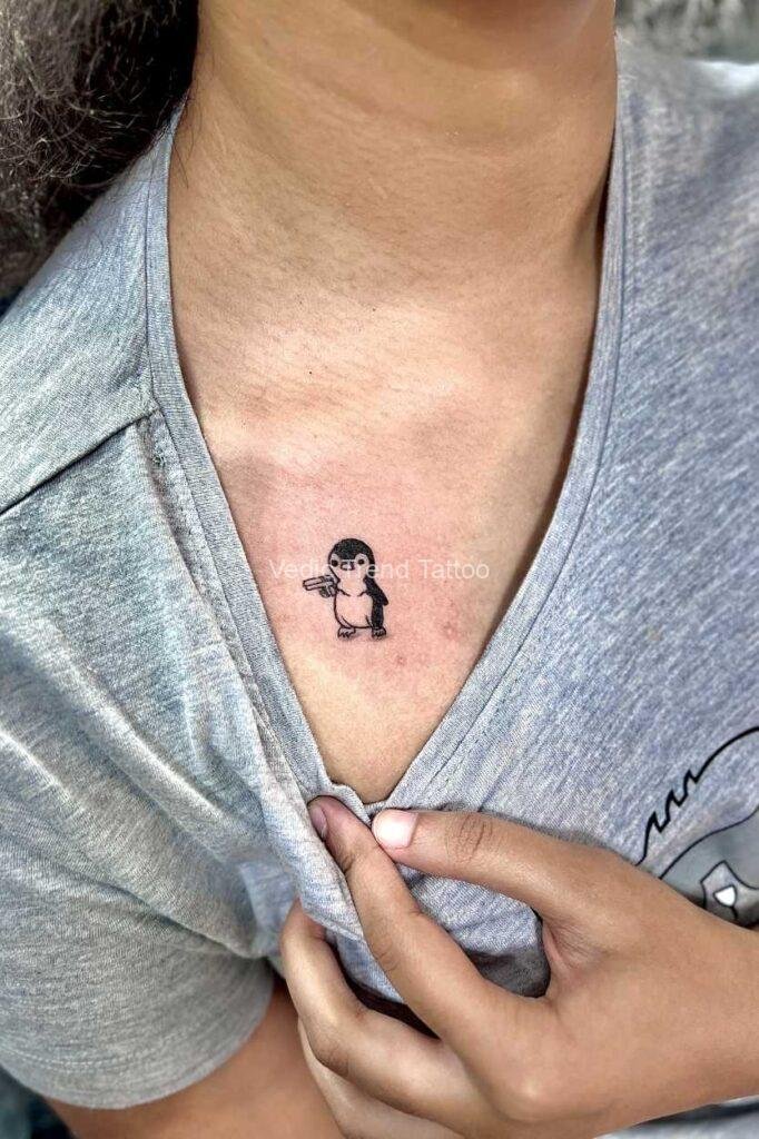 Penguin-bird-holding-gun-tattoo-on-young-girl-chest-tattoo